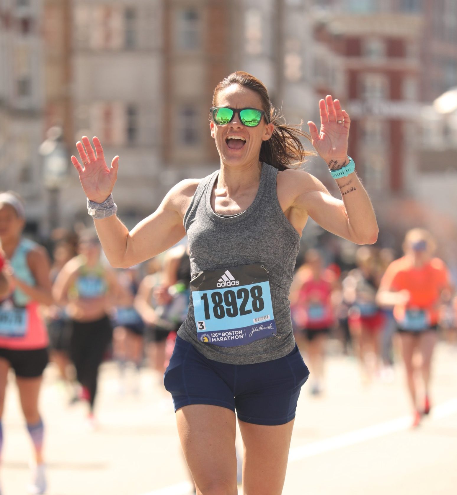 woman running the boston marathon with hands up