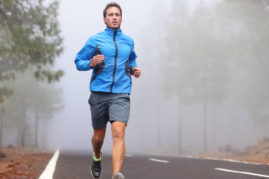 Man wearing a blue jacket running on road in fog